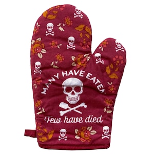 May include: A deep red oven mitt featuring a repeating pattern of white skulls and orange floral motifs. The centre displays a large white skull above crossed bones with the text "MANY HAVE EATEN" arched above and "Few have died" below.