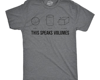 May include: A charcoal gray short-sleeve t-shirt featuring black line drawings of a sphere, a cylinder, and a rectangular prism with their respective volume formulas. Below the shapes, the text reads THIS SPEAKS VOLUMES in black capital letters.
