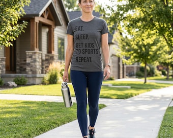 May include: A charcoal gray short-sleeve t-shirt with the black text EAT. SLEEP. GET KIDS TO SPORTS. REPEAT. printed on the front, paired with solid navy blue leggings, gray athletic sneakers, and a silver-toned stainless steel water bottle.