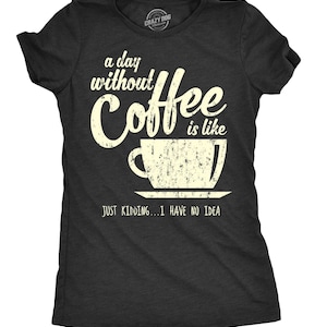 May include: A charcoal grey short-sleeve t-shirt featuring a distressed cream-colored graphic of a coffee cup and the text: a day without Coffee is like JUST KIDDING...I HAVE NO IDEA. The shirt has a crew neckline and a standard fit.