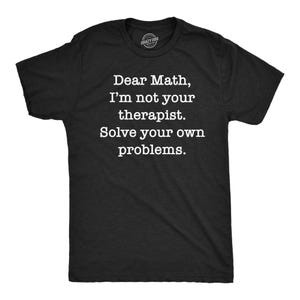 以下が含まれることがあります： 胸元に白い文字で「Dear Math, I'm not your therapist. Solve your own problems.」とプリントされた黒い半袖Tシャツ。クルーネックで標準的なフィット感があり、襟元には小さな円形のロゴが入っています。