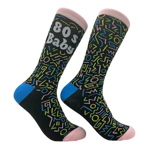 Puede incluir: Un par de calcetines negros con un patrón geométrico colorido de estilo años 80. Un calcetín tiene el texto "80s Baby" en letras blancas.