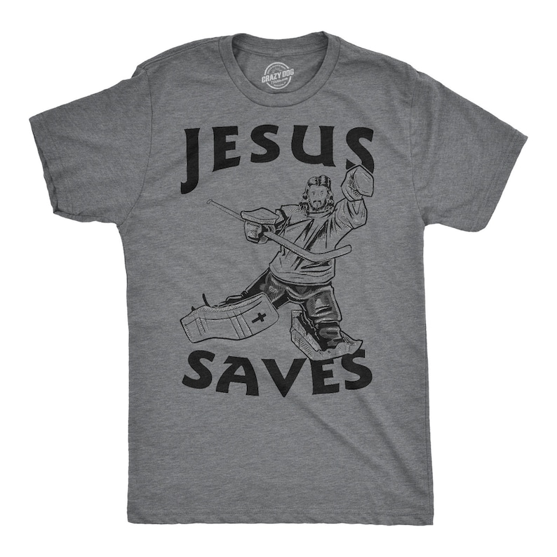 Puede incluir: Una camiseta gris con un gr&aacute;fico negro de un portero de hockey con el texto "JESUS SAVES".