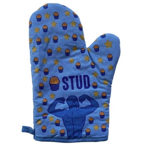 May include: Blue oven mitt with a pattern of yellow stars and brown cupcakes. The mitt has the word "STUD" printed on it in blue letters and a blue silhouette of a person flexing their biceps.