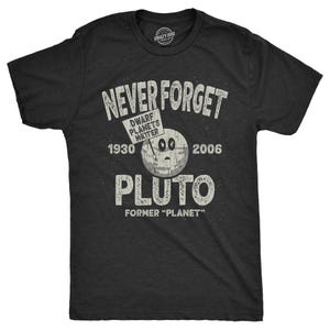 Könnte beinhalten: Ein schwarzes T-Shirt mit einer abgenutzten weißen Grafik, auf der "Never Forget Pluto" steht, mit einem Cartoon-Bild von Pluto und einem Schild mit der Aufschrift "Dwarf Planets Matter". Die Grafik enthält auch die Jahre 1930 und 2006.
