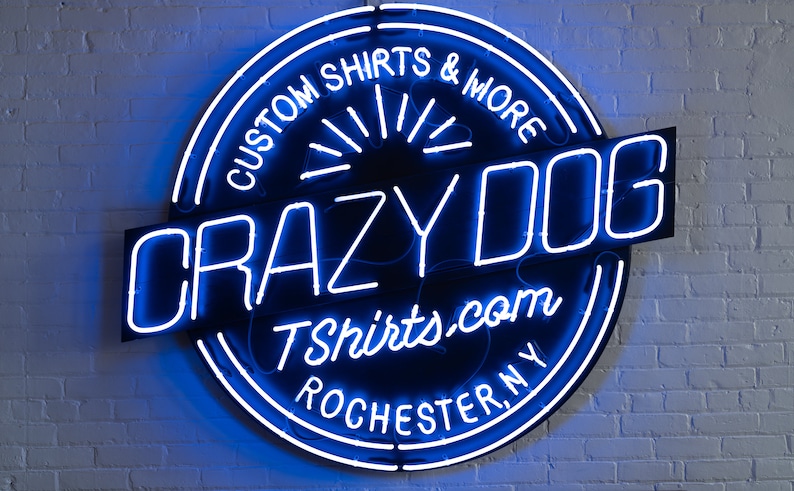 May include: A blue neon sign with a black background that reads "Crazy Dog Tshirts.com Rochester, NY" and "Custom Shirts & More".