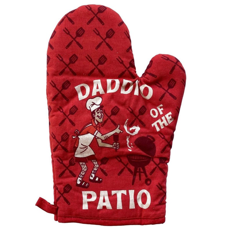 Op de afbeelding: Rode ovenwant met een wit ontwerp van een cartoonkok die grilt en de tekst "Daddio of the Patio".