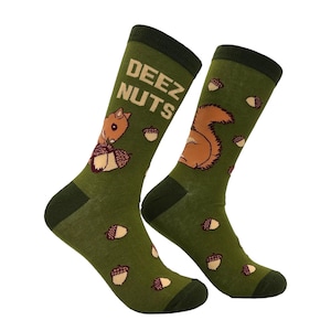 Könnte beinhalten: Ein Paar grüne Socken mit dunkelgrünen Akzenten. Die Socken zeigen ein Cartoon-Eichhörnchen, Eicheln und den Text "DEEZ NUTS" in Weiß. Das Eichhörnchen ist braun und beige und hält eine Eichel.