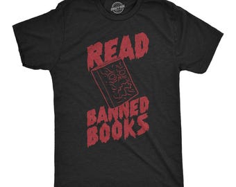 Puede incluir: Una camiseta negra de manga corta con un gráfico rojo de un libro con una cara en la portada. El texto READ BANNED BOOKS está impreso en una fuente roja desgastada encima y debajo de la ilustración del libro. Tiene cuello redondo.