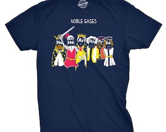 May include: A navy blue short-sleeve t-shirt featuring a graphic of six figures dressed as medieval royalty with periodic table element symbols on their faces. The text NOBLE GASES is printed above the figures, which include Ne, He, Ar, Rn, Kr, and Xe.