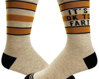 May include: A pair of crew socks in a heathered beige color featuring horizontal mustard yellow and black stripes. The right sock displays the black text IT'S OK TO FART. Both socks have solid black heels and black toes with thin white stripes.
