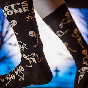 Könnte beinhalten: Schwarze Socken mit einem weißen Skelett-Motiv und dem Text "Let's Bone" in weißen Buchstaben.