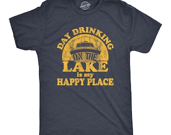 Op de afbeelding: Een donkerblauw t-shirt met korte mouwen en een verweerde gele afbeelding van een boot op het water. De tekst DAY DRINKING ON THE LAKE IS MY HAPPY PLACE staat in een vet, versleten lettertype. Het t-shirt heeft een ronde halslijn.