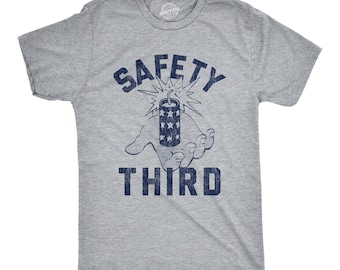 Puede incluir: Una camiseta gris jaspeado de manga corta con un estampado gráfico azul oscuro. El diseño muestra una mano sosteniendo un fuego artificial encendido con estrellas, rodeado por el texto SAFETY arriba y THIRD abajo en una fuente negrita desgastada.