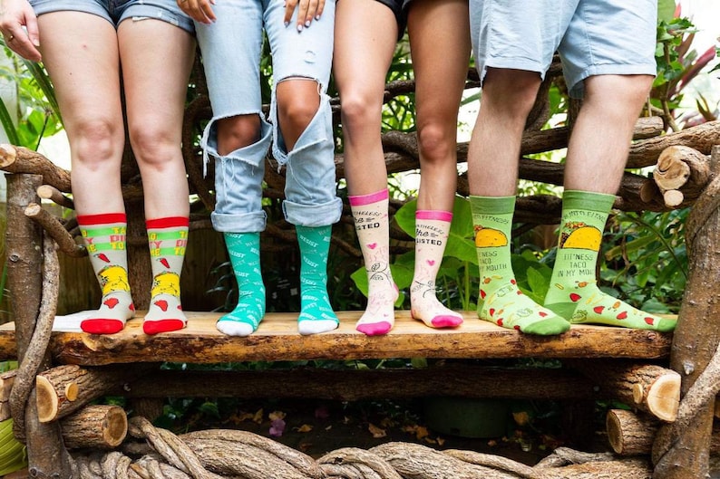 May include: Five pairs of colorful socks with humorous sayings and images. The socks feature a taco, a heart, a chicken, and a green design.
