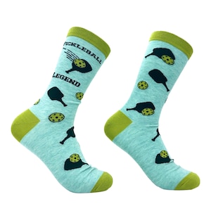 May include: A pair of light blue crew socks featuring a repeating pattern of dark navy pickleball paddles and yellow pickleball balls. The text PICKLEBALL LEGEND is printed in dark navy on the upper portion of the left sock.