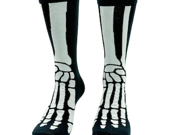 May include: A pair of black crew socks featuring a white graphic print of human foot and leg bones. The design extends from the toe area up to the calf, displaying the metatarsals, phalanges, and lower leg bones in a high-contrast skeletal pattern.