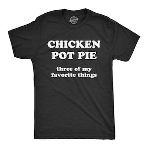 May include: A charcoal gray short-sleeve t-shirt featuring white distressed-style text that reads CHICKEN POT PIE three of my favorite things. The shirt has a crew neckline and a small circular brand logo printed on the inside of the collar area.