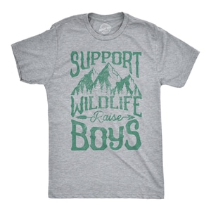 Könnte beinhalten: Ein graumeliertes Kurzarm-T-Shirt mit einem grünen Grafikdruck von Berggipfeln und Tannenbäumen über dem Text "SUPPORT WILDLIFE RAISE BOYS", wobei ein Pfeilsymbol die Wörter "WILDLIFE" und "RAISE" auf der Vorderseite der Brust trennt.