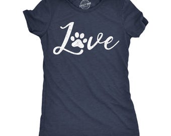 May include: A dark navy blue short-sleeve t-shirt featuring the word Love in a white distressed script font, where the letter o is replaced by a paw print graphic. The shirt has a crew neckline and a label printed inside the collar area.
