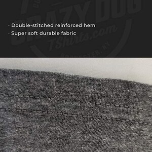 May include: Close-up of a gray t-shirt hem with a double-stitched reinforced hem. The stitching is visible and the fabric appears soft and durable.