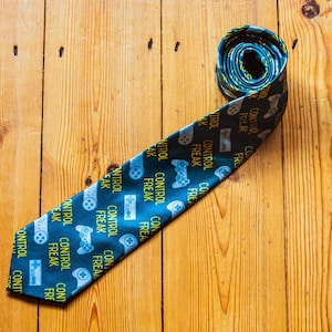 May include: A blue and green patterned tie with the words "Control Freak" repeated on it. The tie is rolled up and lying on a wooden surface.