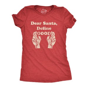 May include: A red short-sleeved t-shirt featuring the white distressed text "Dear Santa, Define GOOD" centered on the chest. Below the text are two white graphic illustrations of hands with fingers crossed, also in a distressed style.