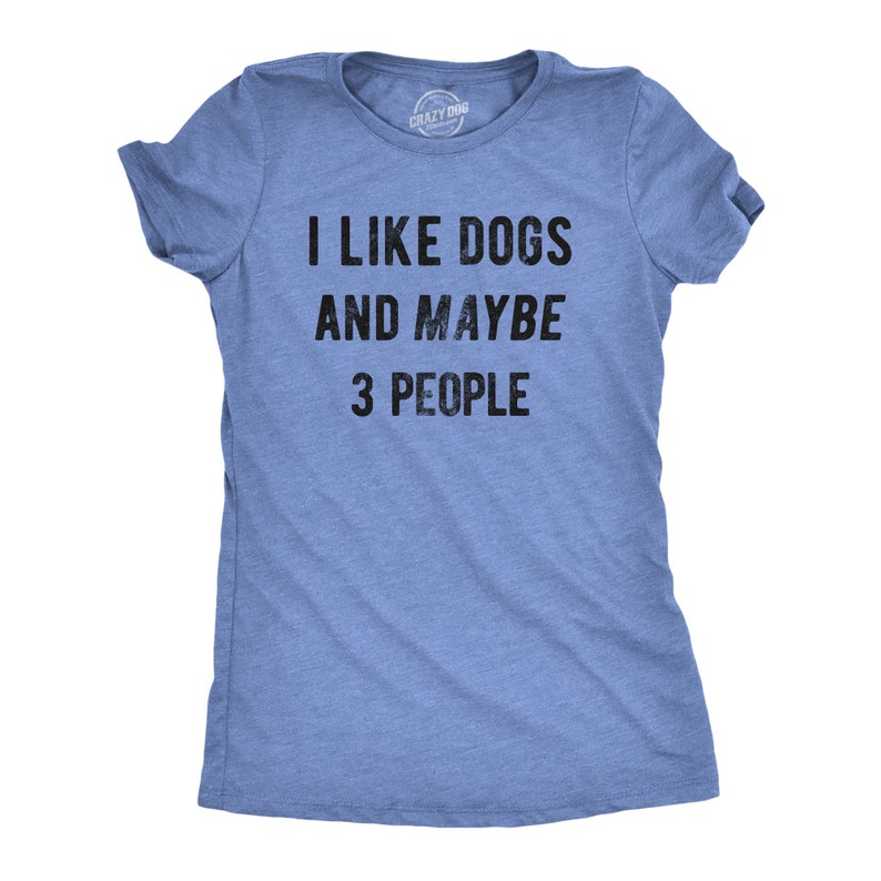 May include: A light blue t-shirt with the text "I LIKE DOGS AND MAYBE 3 PEOPLE" in black. The shirt is made of a soft material and has short sleeves. The Crazy Dog brand logo is visible on the neckline.