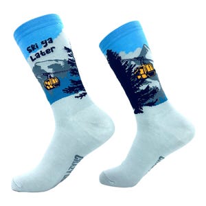 May include: A pair of light blue crew socks featuring a graphic of a yellow ski lift gondola, dark blue pine trees, and a mountain landscape. The left sock includes the black text "Ski ya Later" printed near the top cuff of the garment.