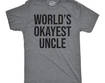 May include: A heather gray short-sleeved t-shirt featuring the black text "WORLD'S OKAYEST UNCLE" printed in a bold, sans-serif font across the chest. The garment has a crew neckline and a standard fit, with a small brand logo inside the collar.