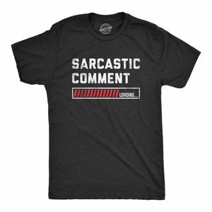 May include: A charcoal gray short-sleeve t-shirt featuring the white distressed text SARCASTIC COMMENT above a red and white loading bar graphic with the text LOADING... inside a rectangular frame on the front of the garment.