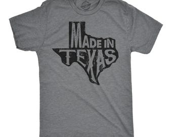 May include: A heather grey short-sleeve t-shirt featuring a black distressed graphic of the state of Texas. The text "MADE IN TEXAS" is printed in a bold, weathered font inside the state outline, centered on the front of the garment.