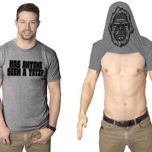 May include: A heather grey t-shirt with the text "Has anyone seen a Yeti?" printed on the front. The t-shirt has a hidden design that reveals a Yeti face when the shirt is pulled up over the head.
