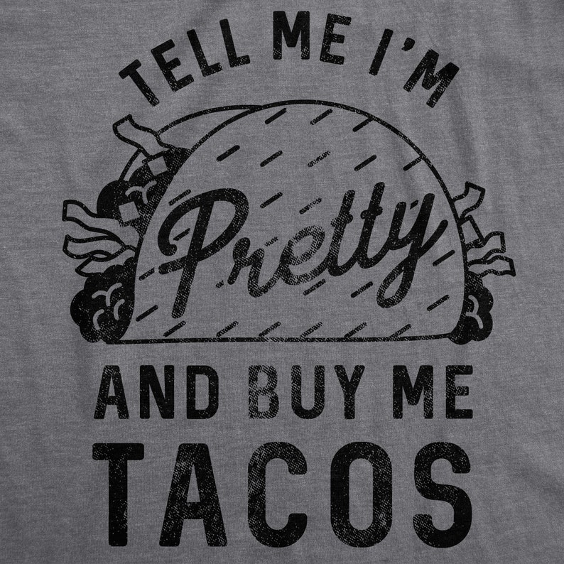 May include: A gray t-shirt with black text that reads "Tell me I'm pretty and buy me tacos". The text is stylized to look like a vintage design. A black and white illustration of a taco is in the center of the text.
