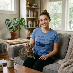 May include: A heather blue short-sleeve t-shirt featuring a dark blue graphic of a cat with a unicorn horn. The text reads: I WAS LIKE, "WHATEVER BITCHES AND THE BITCHES WHATEVERED". The shirt has a crew neckline and a soft, heathered texture.