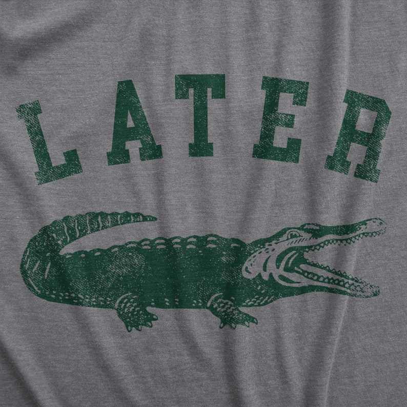 May include: Gray t-shirt with a distressed green graphic of an alligator and the word "LATER" above it. The alligator is detailed with open jaws, and the text has a vintage, worn look.