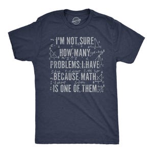 May include: A navy blue short-sleeve t-shirt featuring white distressed text that reads I'M NOT SURE HOW MANY PROBLEMS I HAVE BECAUSE MATH IS ONE OF THEM, surrounded by various mathematical formulas, geometric triangles, and algebraic equations.