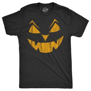 May include: Black t-shirt with a distressed orange jack-o'-lantern face graphic. The graphic is a simple, stylized face with a wide grin and two eyes.