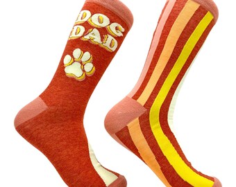 May include: A pair of crew socks with a rust-colored base. One sock features the text DOG DAD in white letters above a white paw print. The other sock displays vertical stripes in shades of pink, orange, yellow, and cream along the side.