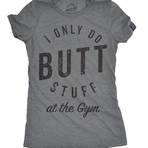 May include: A charcoal grey short-sleeve t-shirt featuring the black distressed text I ONLY DO BUTT STUFF at the Gym printed on the front. The shirt has a crew neckline and a fitted silhouette with a small brand logo inside the collar.