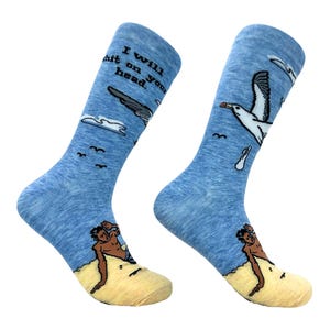 Könnte beinhalten: Ein Paar hellblaue, melierte Crew-Socken mit einer Grafik einer Möwe, die über einer Person an einem Sandstrand fliegt. Der Text "I will shit on your head" ist auf dem oberen Teil der Socken aufgedruckt, ergänzt durch Wolken und Vögel.