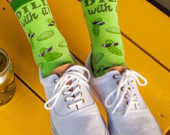 May include: Light green crew socks featuring a repeating pattern of pickles wearing black sunglasses and the text "DILL with it!" in dark green. The socks are worn inside white lace-up sneakers with metallic eyelets and white laces.