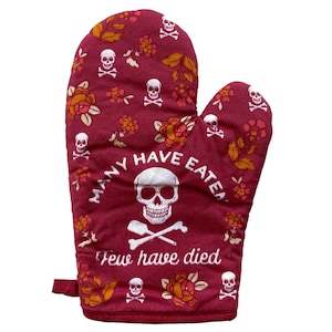 May include: A deep red oven mitt featuring a repeating pattern of white skulls with crossbones and orange floral motifs. The centre displays a large white skull above crossed bones with the text "MANY HAVE EATEN" above and "Few have died" below.