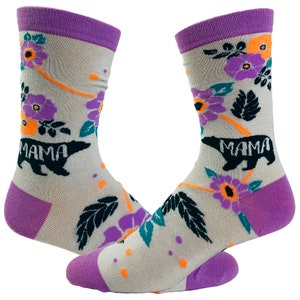 May include: A pair of grey socks with a purple cuff. The socks feature a floral pattern with orange, purple, and teal flowers. The socks also have a black bear silhouette with the word "MAMA" printed on it.