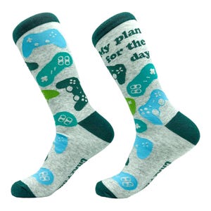 Peut inclure: Une paire de chaussettes mi-mollet gris clair avec un motif répétitif de manettes de jeu vidéo dans des tons bleu, sarcelle et vert foncé. Les chaussettes ont des bords, talons et pointes vert foncé. Le texte "My plans for the day" est imprimé.