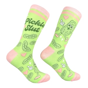 May include: A pair of light green crew socks featuring a repeating pattern of pickles, small pink hearts, and a cartoon pickle character wearing shoes. The text "pickle Slut" is printed in dark green on the upper portion of the socks.