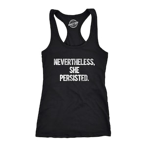 May include: A black racerback vest top featuring the white distressed text "NEVERTHELESS, SHE PERSISTED." printed on the front. The garment has a scoop neckline and a sleeveless design with a brand logo printed on the inside neck label area.