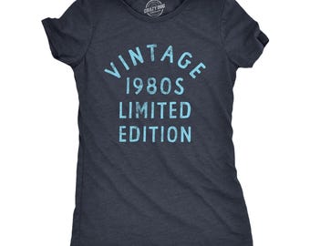 May include: A dark navy blue short-sleeve t-shirt featuring the light blue distressed text VINTAGE 1980S LIMITED EDITION printed on the front. The shirt has a crew neckline and a soft, heathered fabric texture throughout the entire garment.