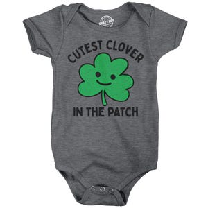 May include: A gray baby onesie with a green four-leaf clover with a smiling face and the text "Cutest Clover in the Patch".