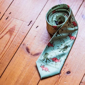 May include: A green silk tie with a pattern of pink dinosaurs and the text "DADASaurus".